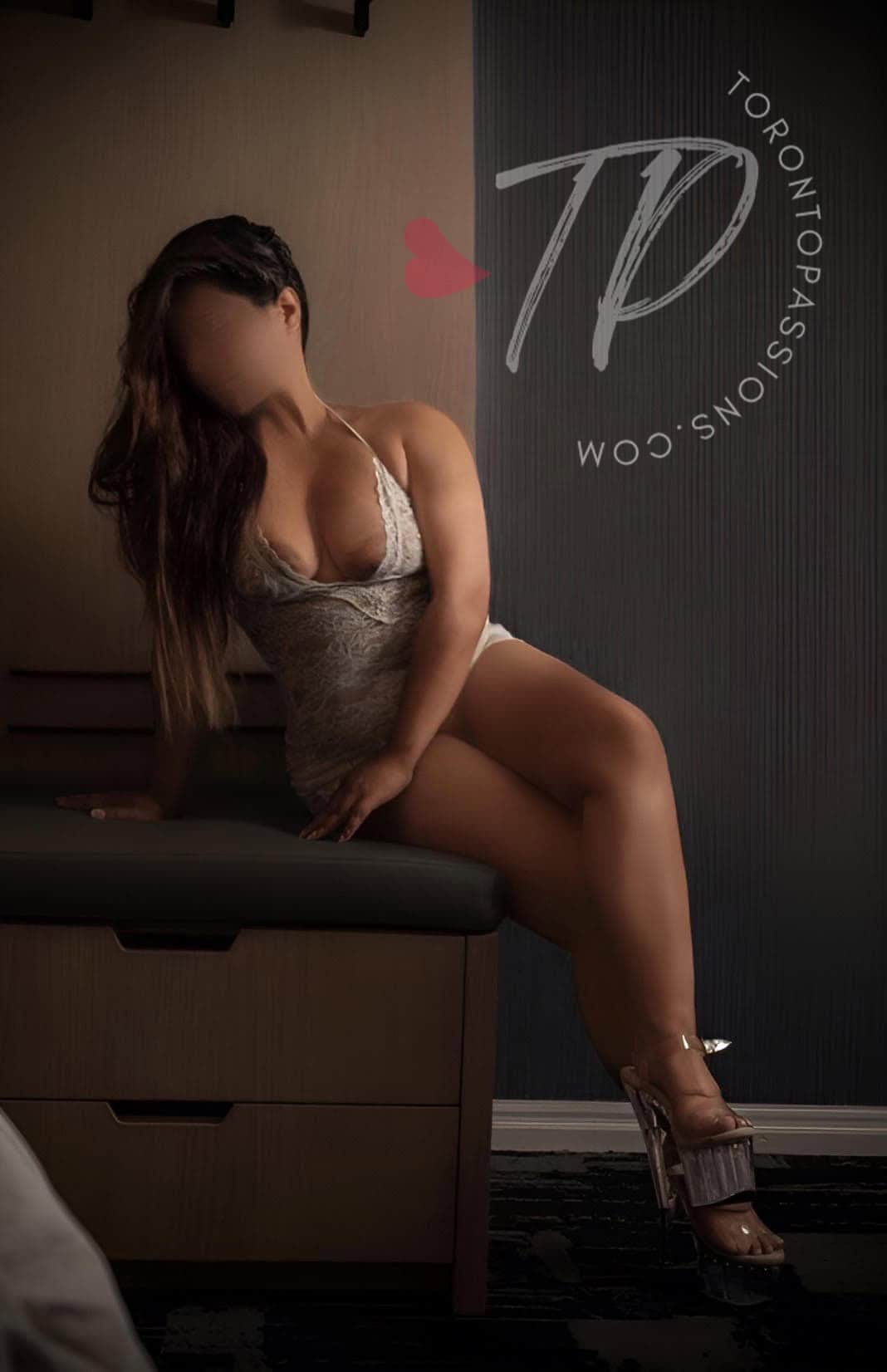 Amira posing in lingerie leaning on a table.