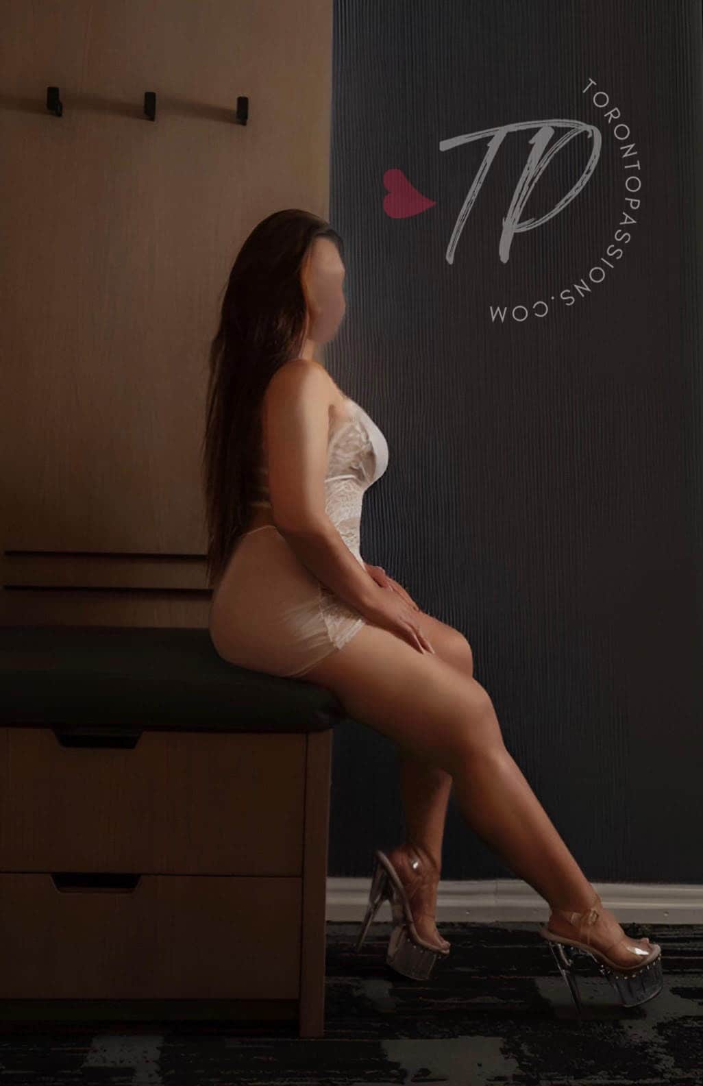 Profile of Amira seated in lingerie and heels.