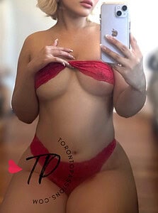 Woman in red lingerie taking mirror selfie with iPhone.