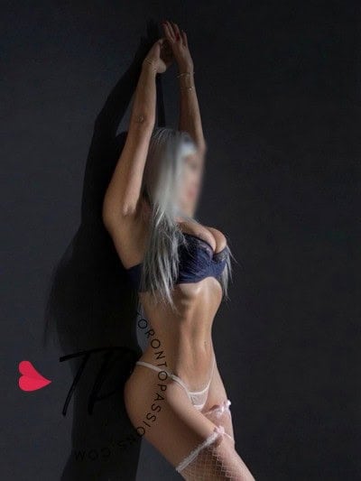 Elegant woman in lingerie with arms raised against dark background.
